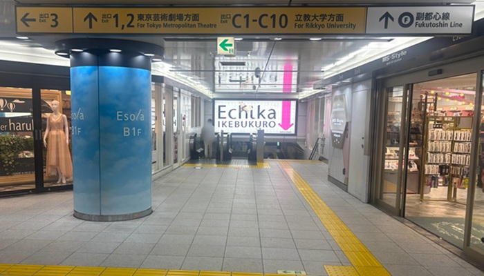 池袋駅地下通路。「↑出口1,2 東京芸術劇場方面」の案内板と青空模様のEsolaの柱があり、奥にあるEchika(エチカ)へ下るエスカレーター