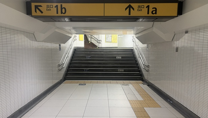 池袋駅の1b出口直前にある階段。「↖出口1b」「↑出口1a」と書かれた黄色の案内板と地上へ続く階段